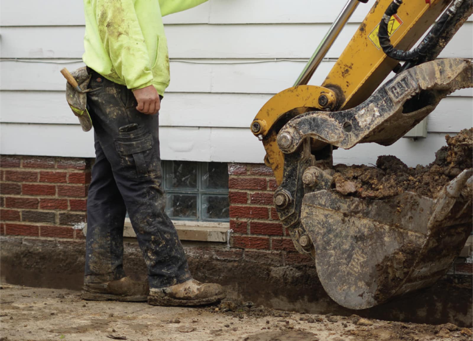 Worker and excavator beside an exposed residential foundation.