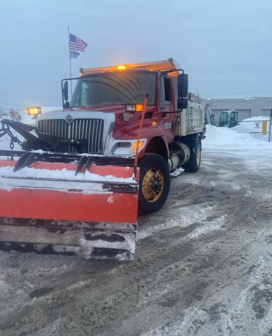 Red snowplow truck clearing a commercial property
